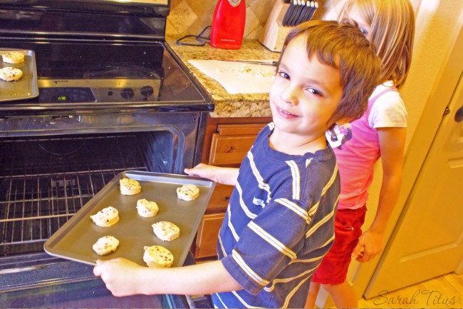 Little boy putting cookies in the oven to bake