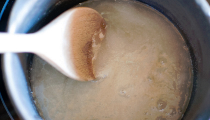 Stirring sugar, honey and water in a pan with a wooden spoon
