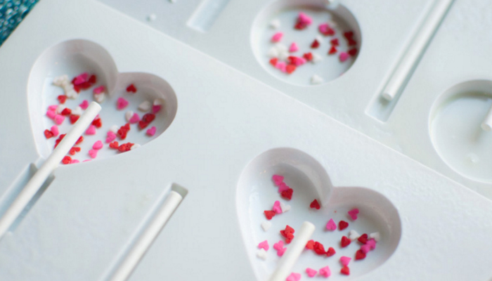White heart shaped sucker molds with pink, red and white sprinkles and a sucker stick in them
