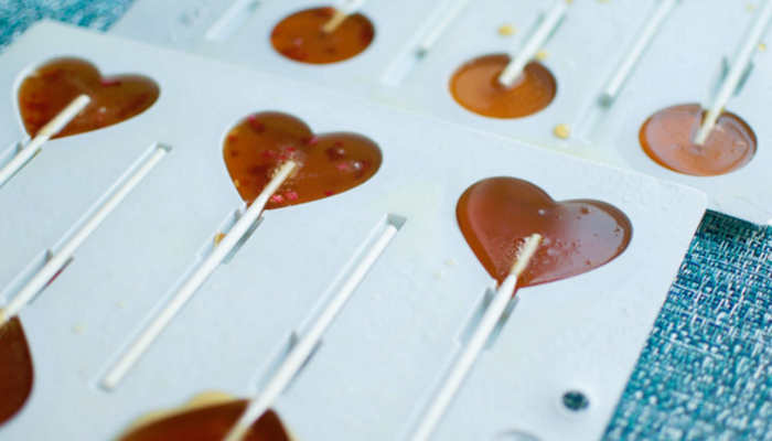 White heart shaped sucker molds filled with sugar and honey mixture.