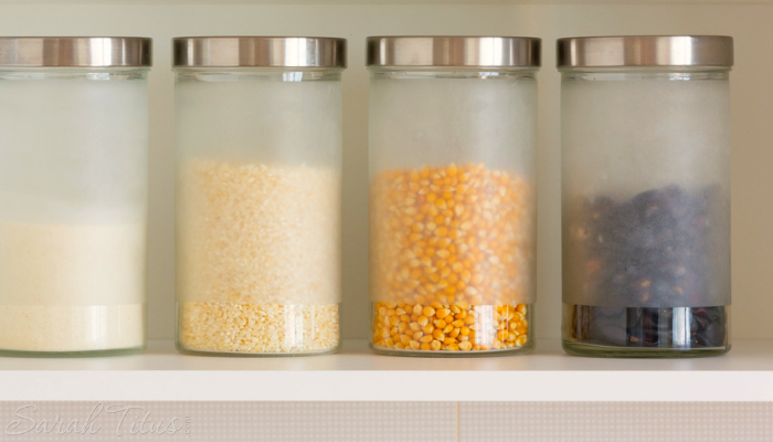 How to Start Decluttering - Frosted glass canisters on a white kitchen shelf filled with grains and seeds