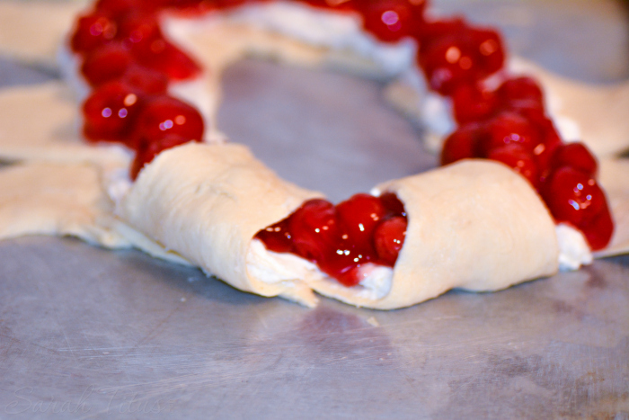 The crescent roll dough spread with the cherry pie filling started to be folded over to make the ring