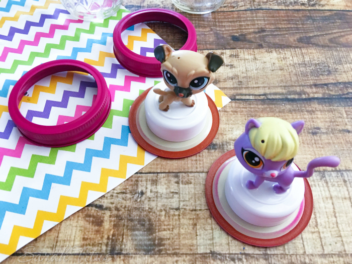  The glued bottle lids glued to fuchsia mason jar lids sitting on a wood table