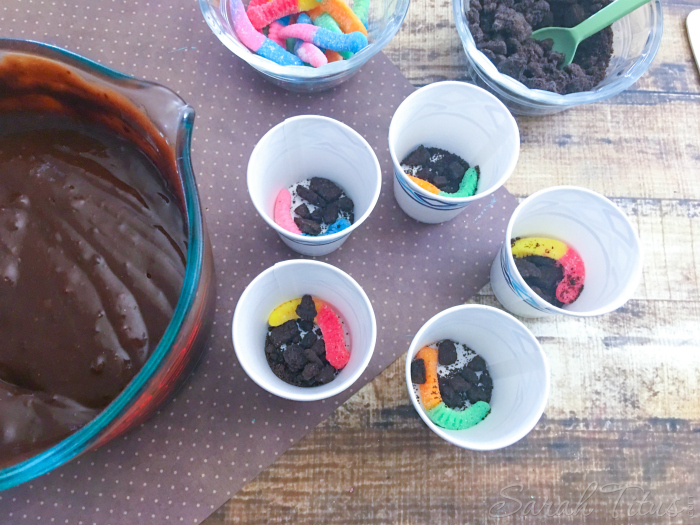 Sprinkling crushed oreo cookies on top of the gummy worm in each Dixie cup