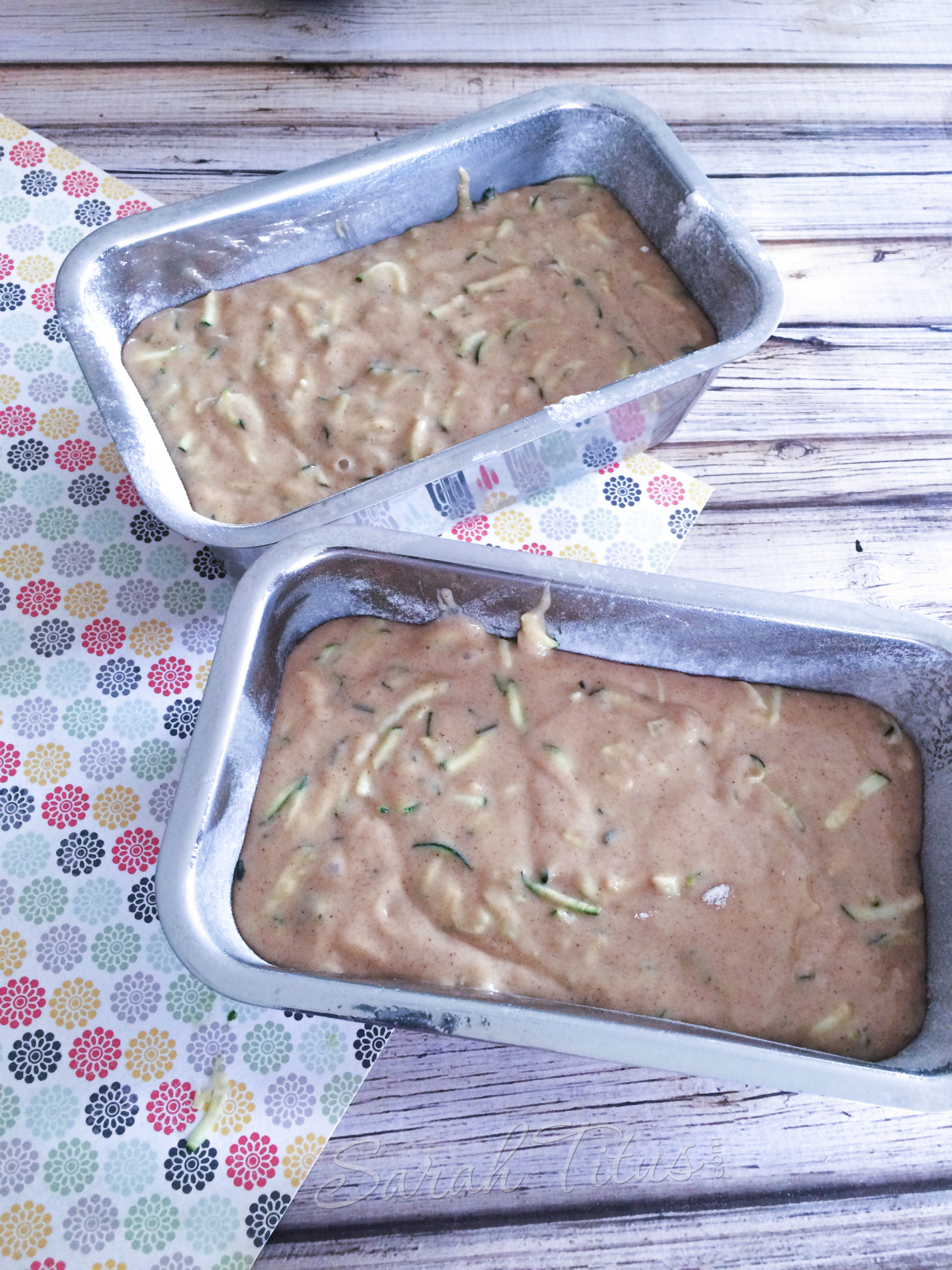 Zucchini Bread batter poured into 2 bread pans sitting on a wood table