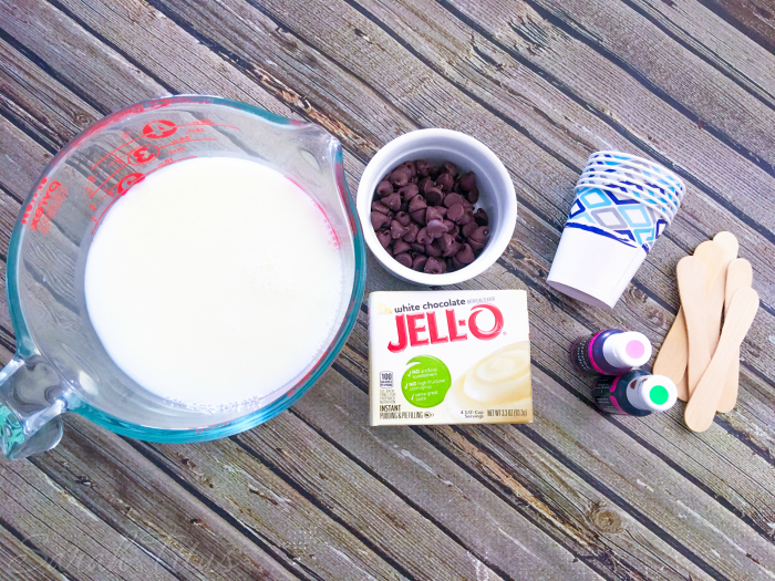 Watermelon pudding pops ingredients: milk, vanilla pudding, chocolate chips, food coloring, popsicle sticks and Dixie cups