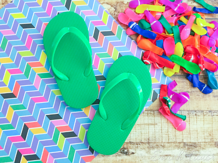 Green child's flip flops on a wooden table with a pile of all different colored balloons in a pile on the side