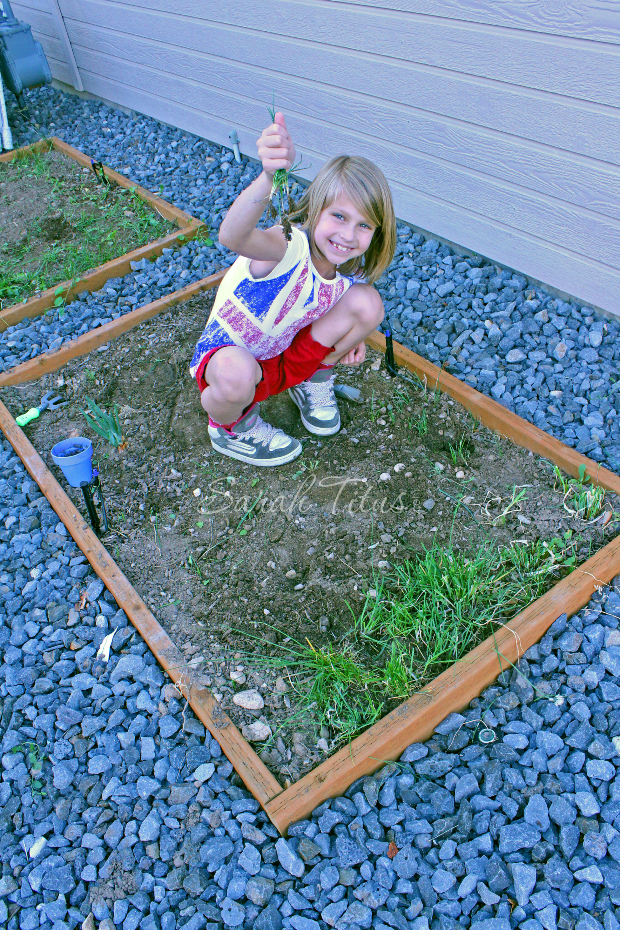 Child pulling weeds out of a rectangle garden bed