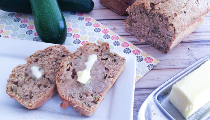 Zucchini Bread on a white plate with butter and fresh zucchinis on the side