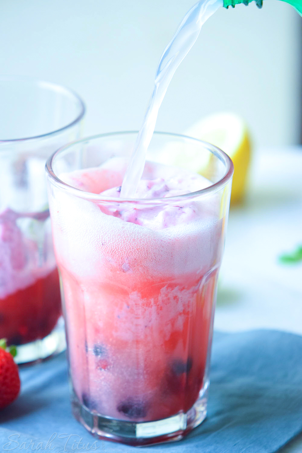 Pouring lemon lime soda over berries, strawberry juice and ice cream in glasses