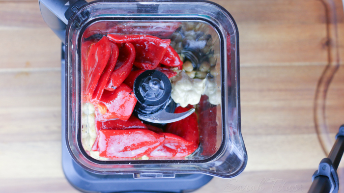 Blender on counter top with roasted red peppers and other hummus ingredients ready to blend