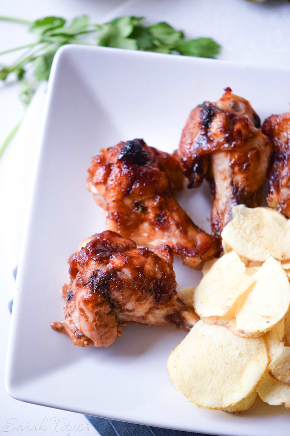 Fully cooked Sweet and Spicy Chicken Wings on a white plate with a side of potato chips all sitting on a blue cloth