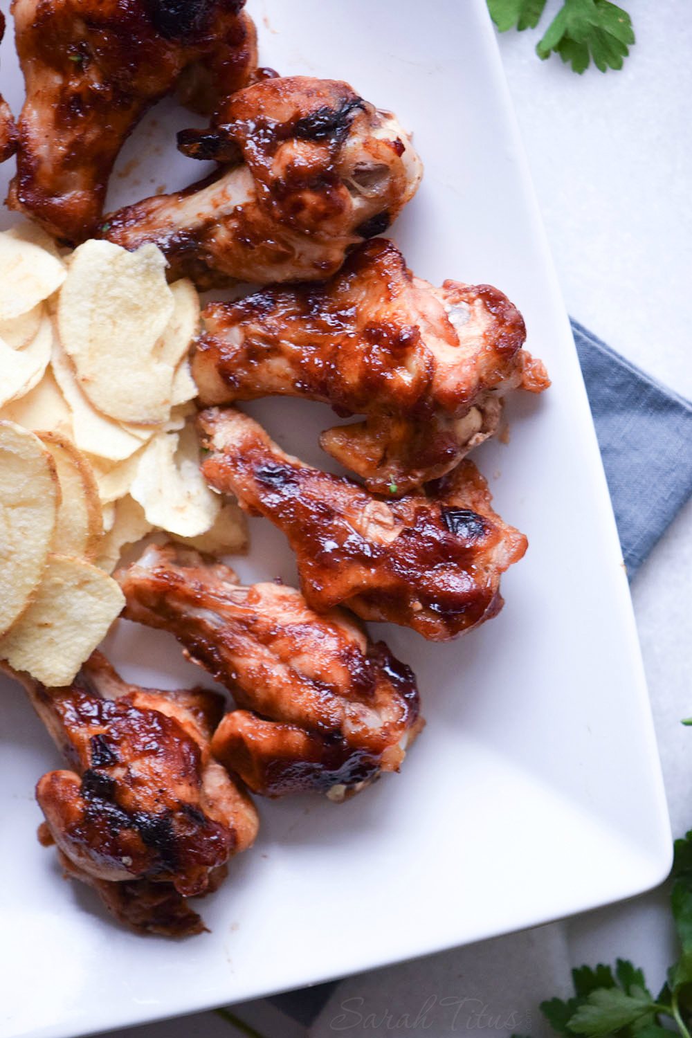 Fully cooked Sweet and Spicy Chicken Wings on a white plate with a side of potato chips all sitting on a blue cloth