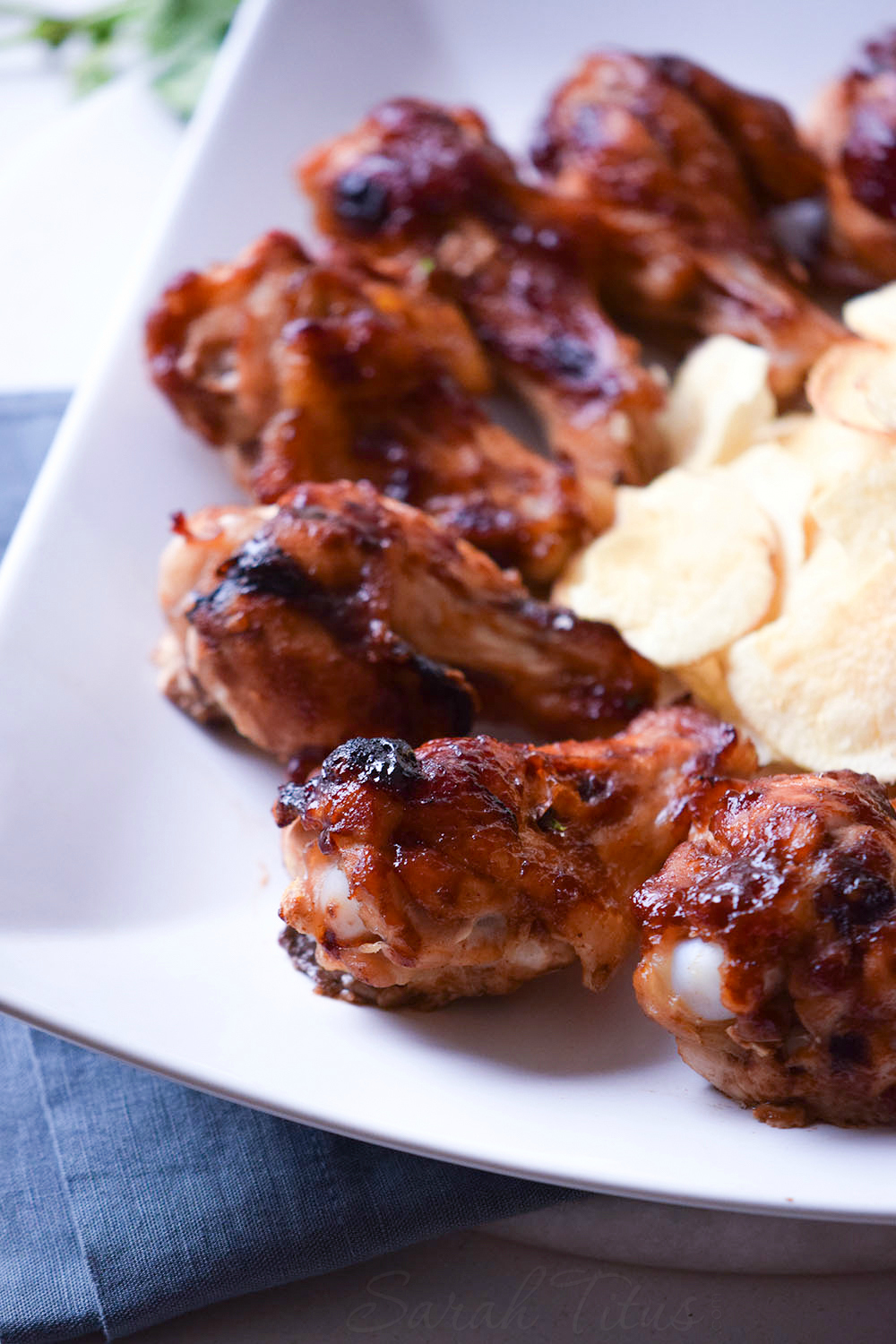 Fully cooked Sweet and Spicy Chicken Wings on a white plate with a side of potato chips all sitting on a blue cloth