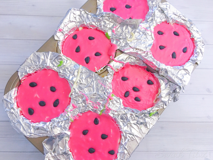 Pink layer of candy melts added to top of Watermelon Fudge and sprinkled black fondant "seeds" in a muffin tin
