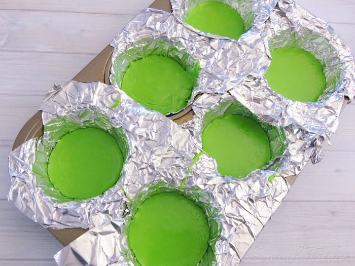 Green melting candy mixture poured into foil lined muffin mold tin