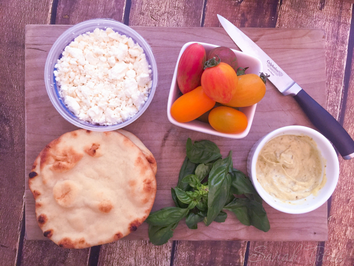 Ingredients for Mini Naan Pizza on cutting board: mini naan bread, Feta cheese, tomatoes, basil and pesto