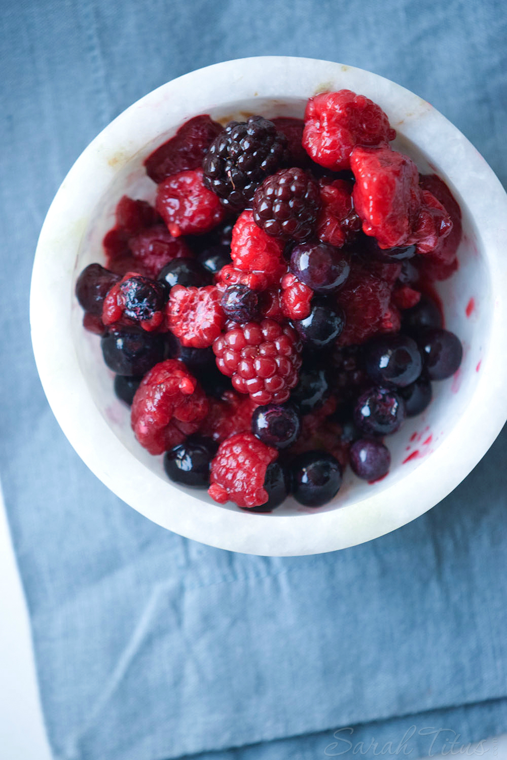 White container of raspberries, blueberries, and blackberries on a blue cloth 