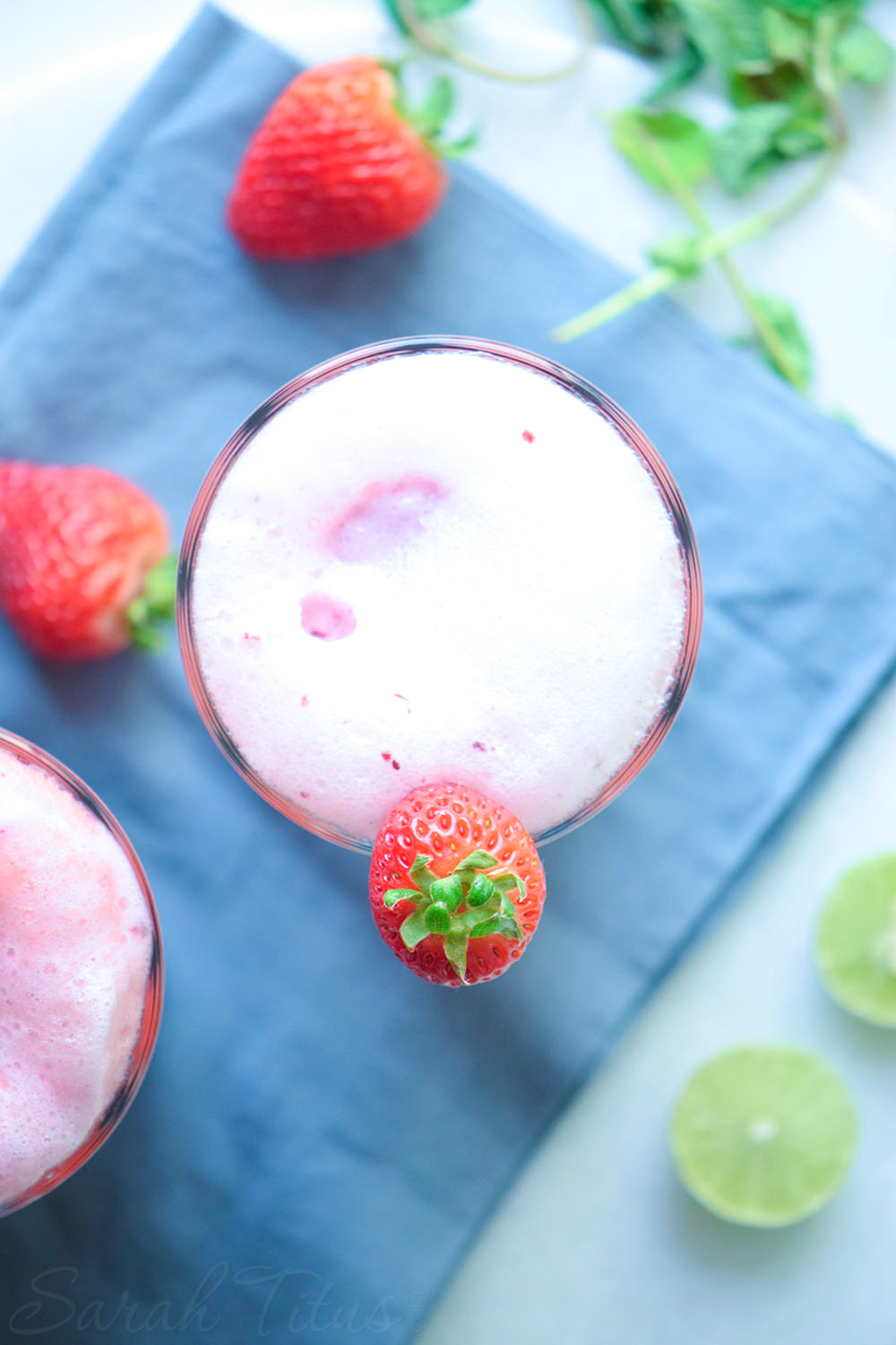 Beautiful frosty glass of Very Berry Ice Cream Float garnished with strawberries sitting on a blue cloth with greenery