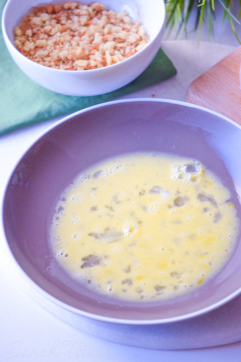 Stirred egg mixture in a purple bowl and seasoned bread crumb mixture in a white bowl for the chicken tenders