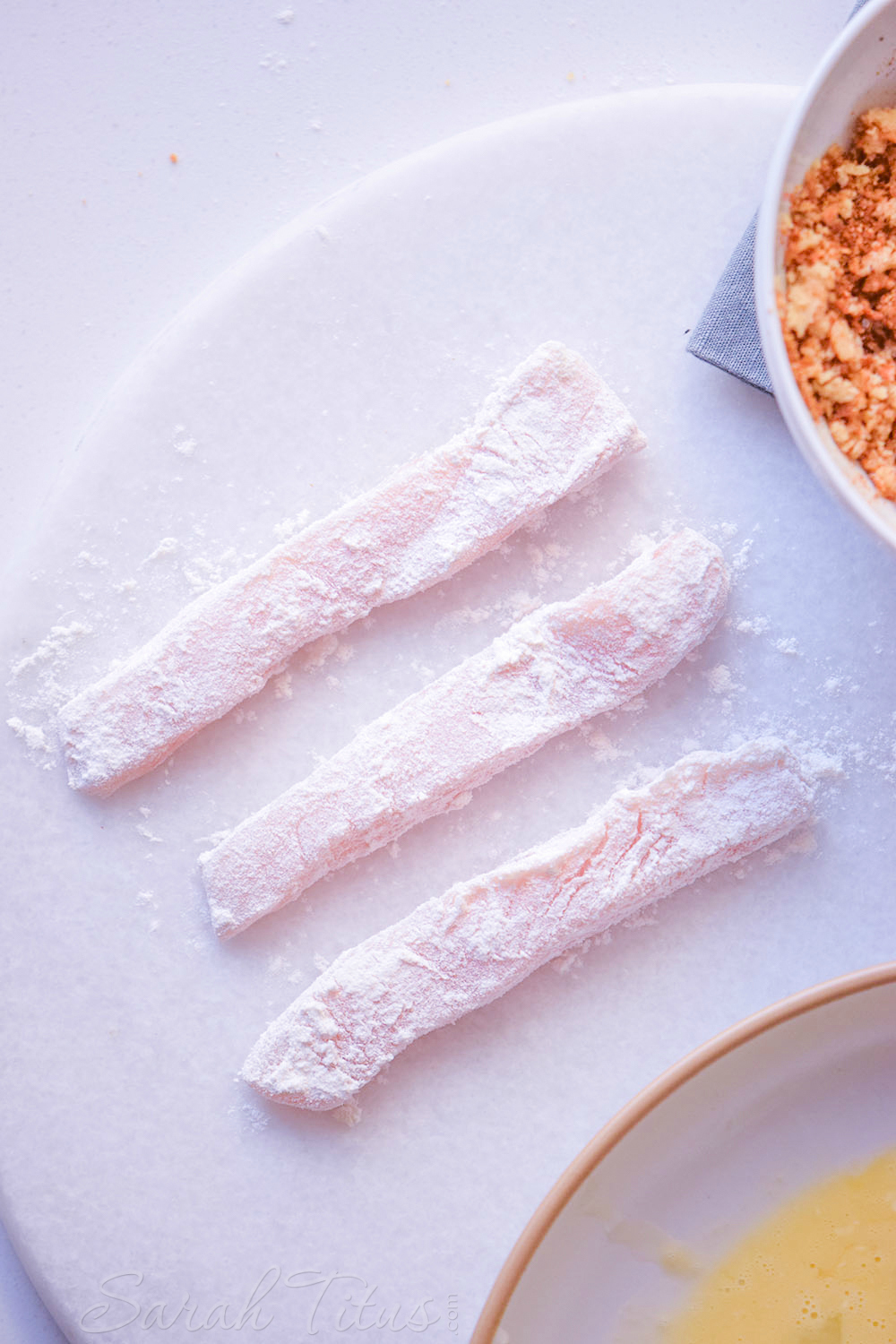 The sliced chicken breast pieces covered with flour on a white plate