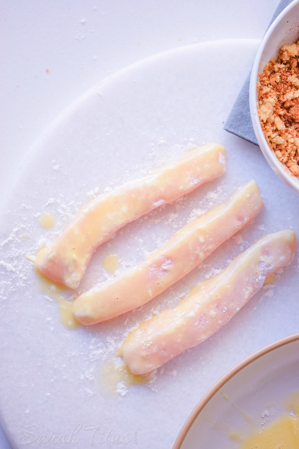 The sliced chicken pieces dipped in egg wash with seasonings on the side