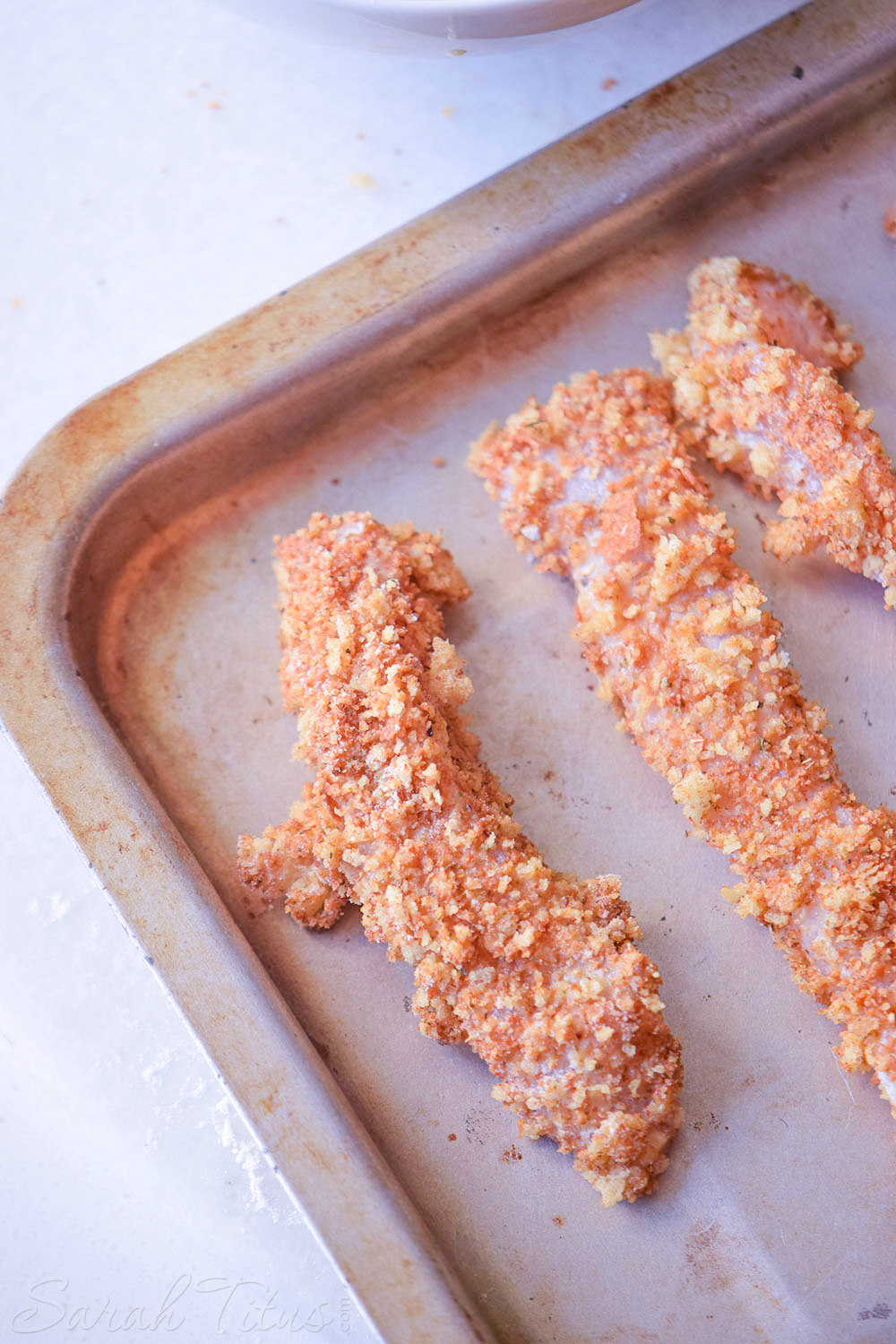 The coated chicken tenders laying out ready to bake on a sheet pan