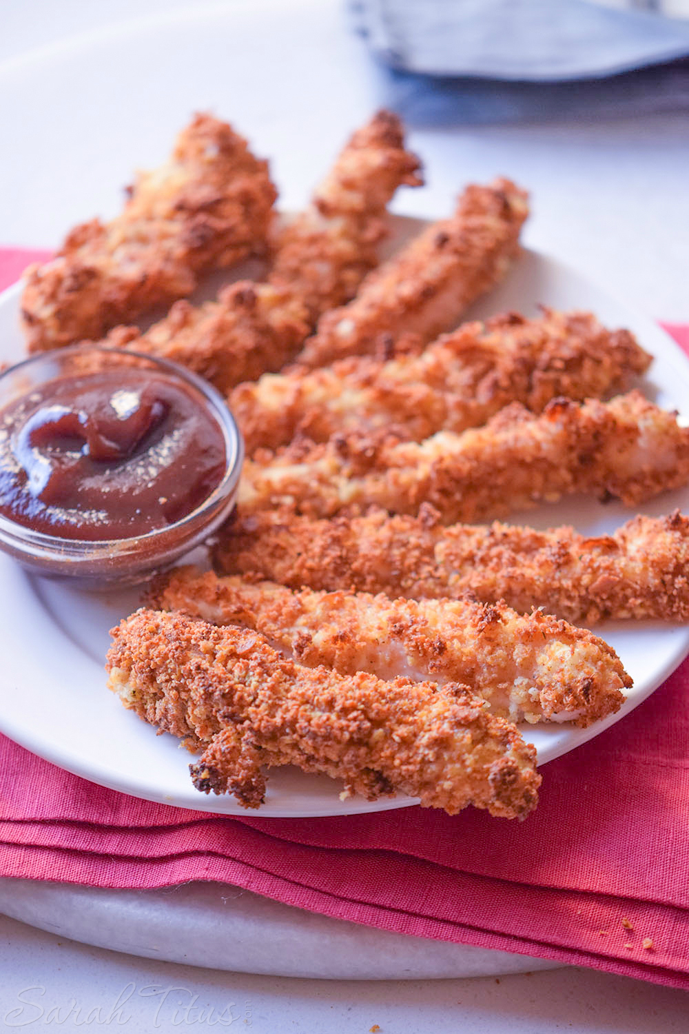 Delicious looking baked chicken tenders on a white plate with a dipping sauce on the side