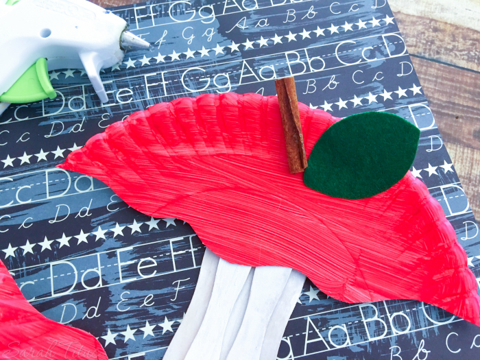 Gluing leaf and cinnamon stick to top of apple craft