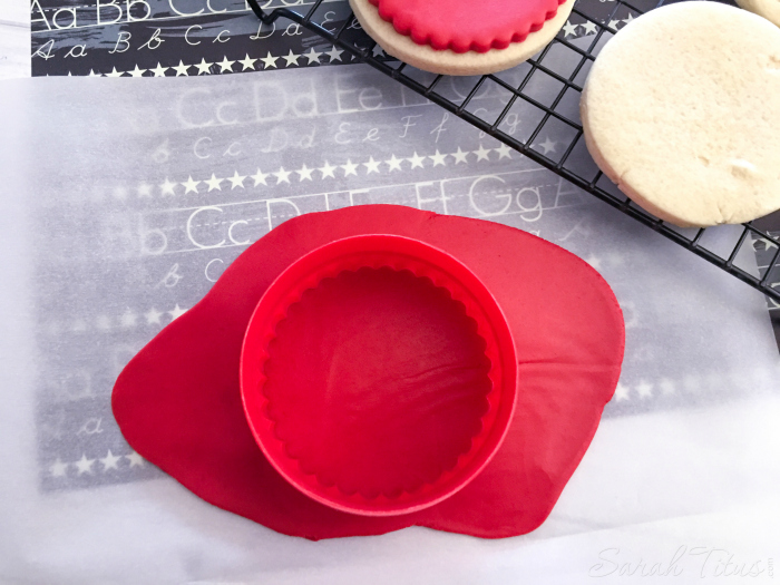 Cutting red fondant with fluted round cookie cutter to place on top of baked cookies