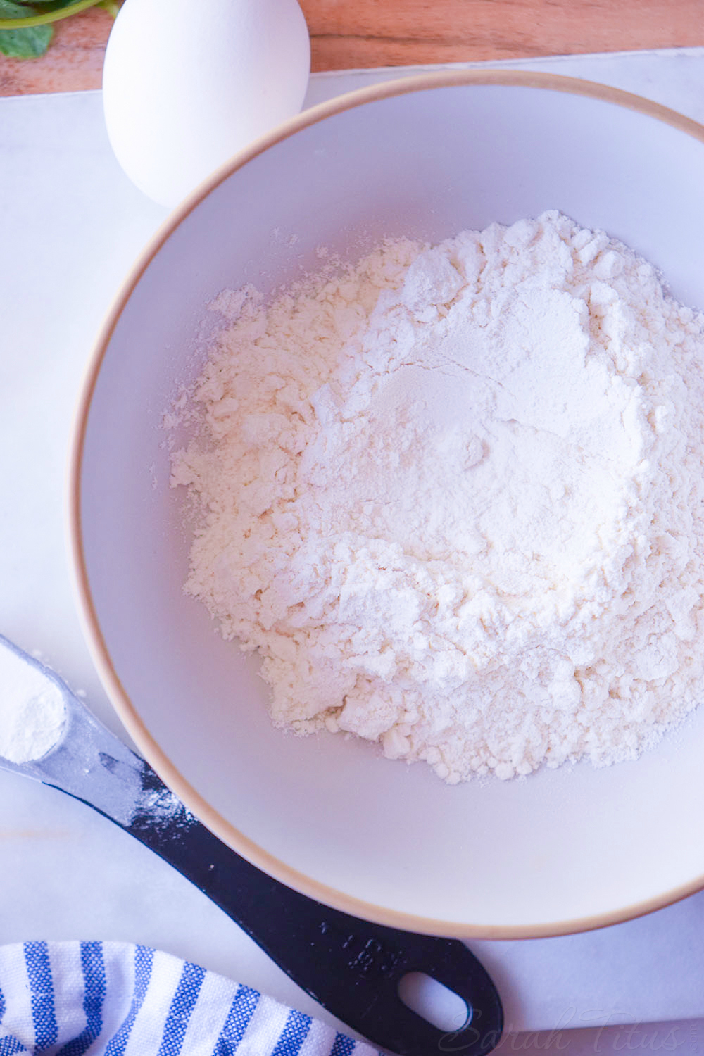 Bowl of flour with an egg and measuring spoon off the side in preparation for making pizza waffles