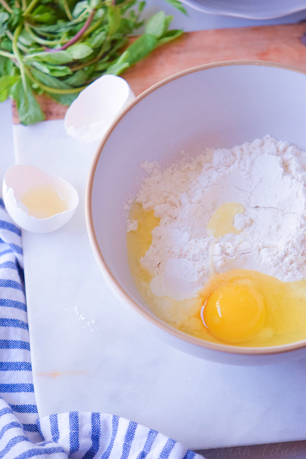 Cracked egg poured over flour in bowl sitting on a cutting board 