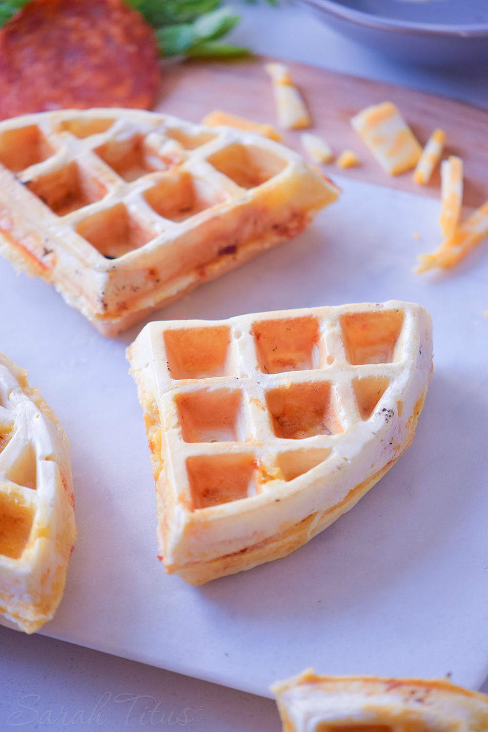 Pizza waffle triangles on a cutting board with cheese and pepperoni on the side