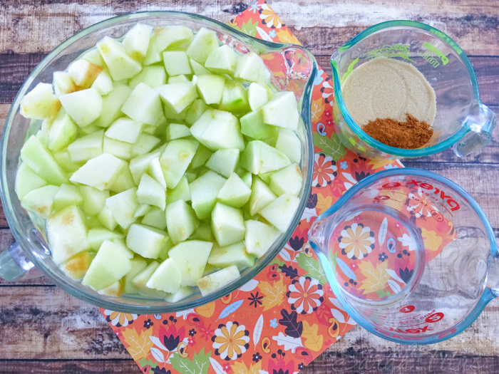 Sliced green apple in a glass measuring cup with cinnamon and sugar in another glass measuring cup and water in a glass measuring cup