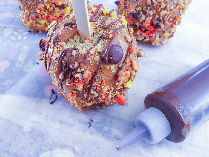 Covering caramel apple with Reese's pieces pieces and drizzling with chocolate sauce