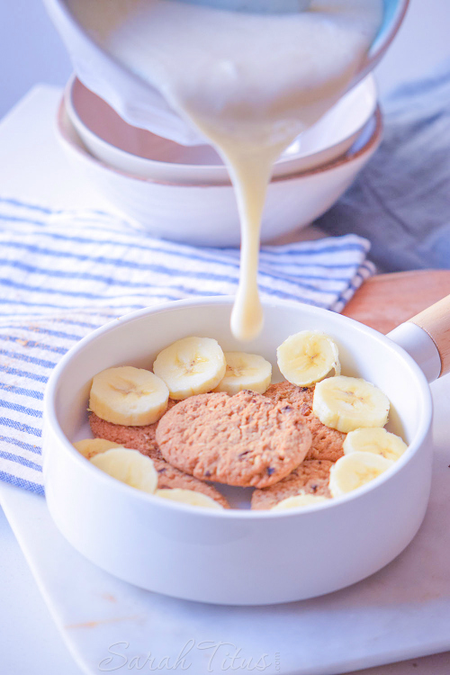 Pouring the cooked banana pudding mixture over top of the cookies and sliced bananas