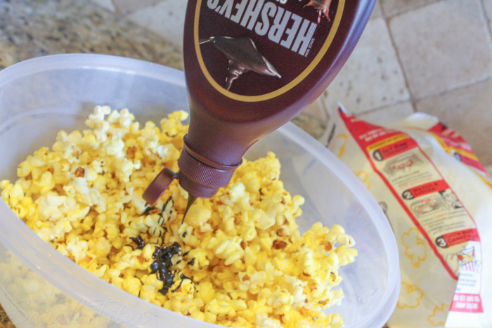 Drizzling chocolate syrup over popcorn in a large plastic bowl