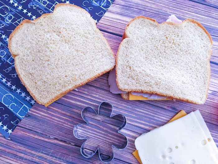 Bread, turkey and cheese laid on a cutting board with a flower shaped cookie cutter and alphabet napkin