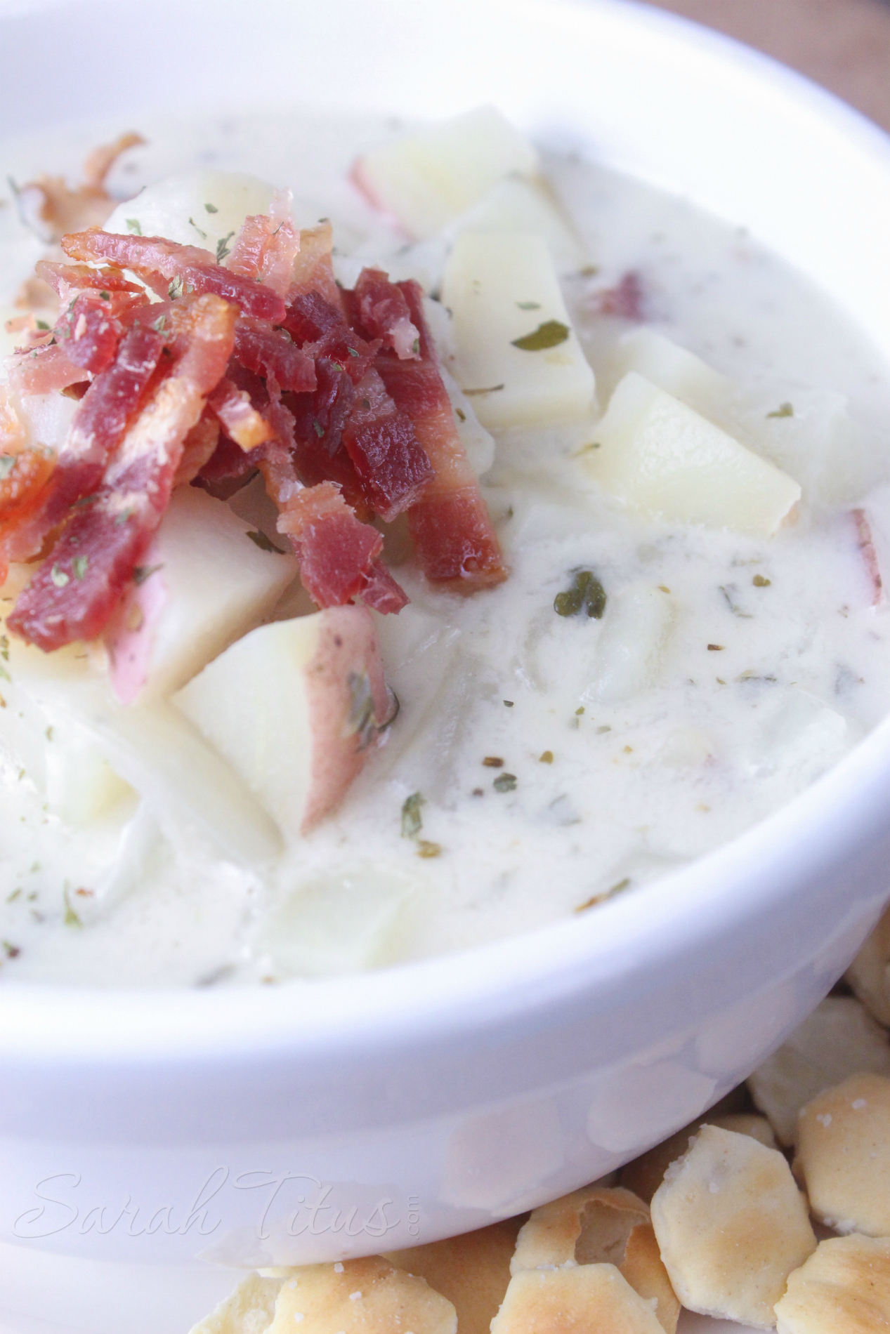 Finished cooking World's Best Clam Chowder in a white bowl topped with potatoes and bacon pieces