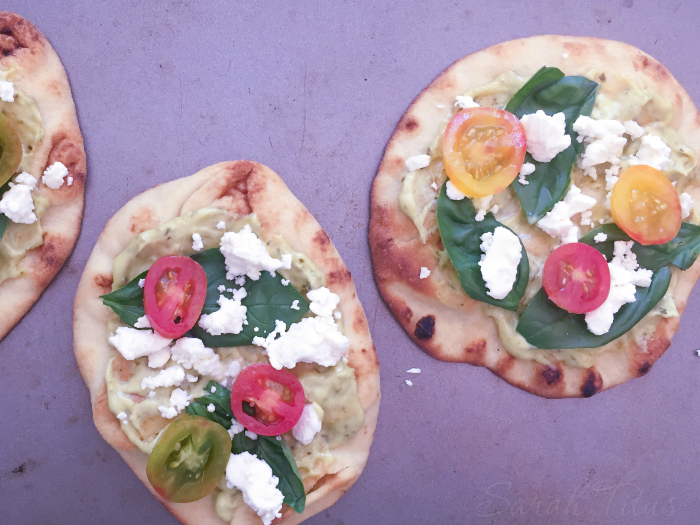 Placing the sliced tomatoes on top of the Feta cheese for the mini Naan pizzas