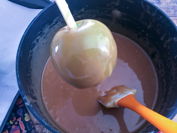 Granny Smith apple on a stick being dipped in caramel sauce
