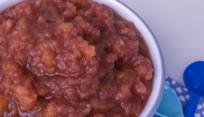 Delicious crockpot applesauce in a white bowl with blue spoon