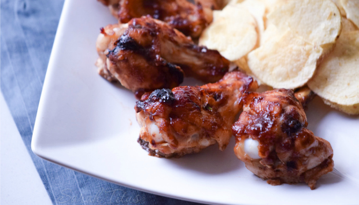 Fully cooked Sweet and Spicy Chicken Wings on a white plate with a side of potato chips all sitting on a blue cloth