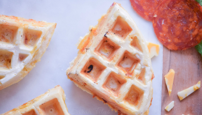 Pizza waffle triangles on a cutting board with cheese and pepperoni on the side