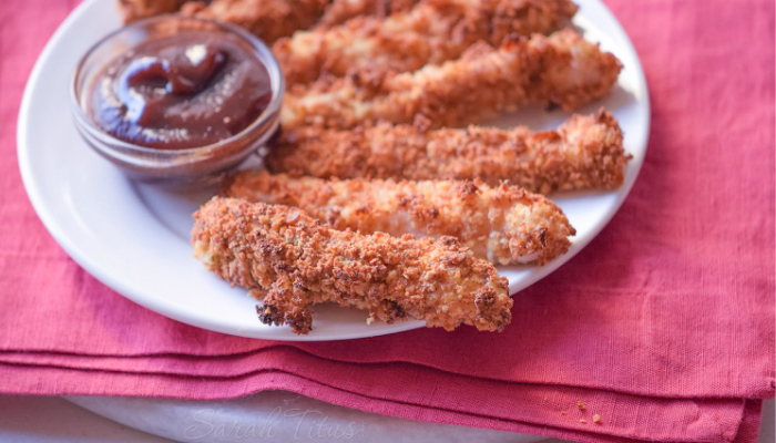 Crowd favorite chicken tenders on a white plate on a pink towel with a dipping sauce
