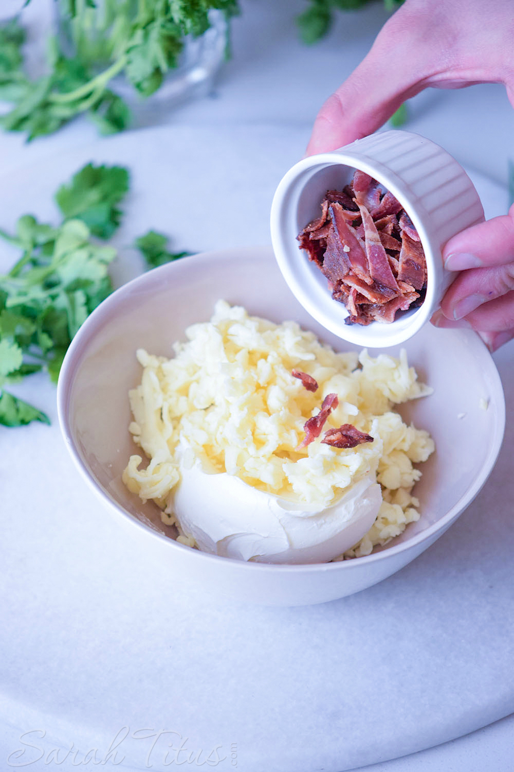 Mini Stuffed Potato Bites - Pouring bacon into a white bowl with the chives, garlic cloves, cream cheese and shredded mozzarella cheese