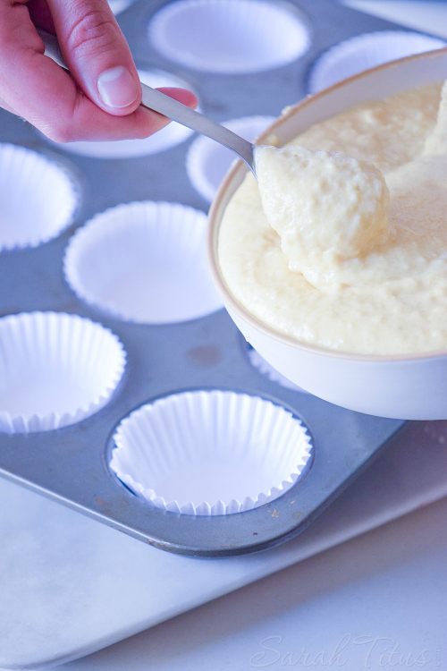 Nutella Swirl Muffins batter being scooped into a metal muffin tin lined with white cupcake papers