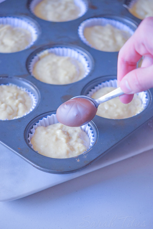 Spoonful of Nutella over muffin batter in a muffin tin