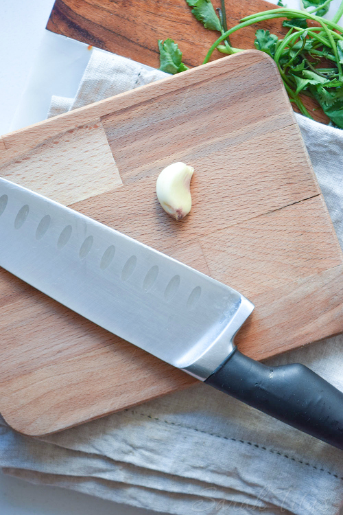 Garlic and chopping knife on a wooding cutting board to chop with spinach on the side