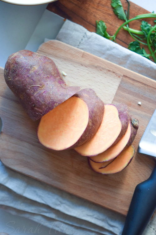 Sweet potato on wooden cutting board partially chopped up with spinach resting on the side